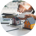 A hand holds a calculator next to a small house model